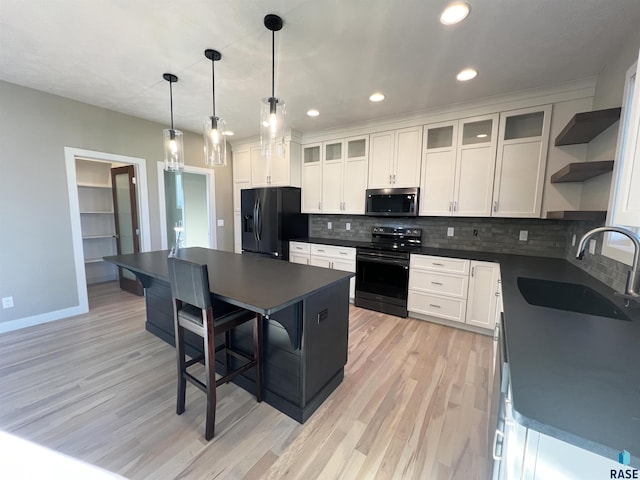 kitchen with pendant lighting, black appliances, white cabinets, sink, and a kitchen island