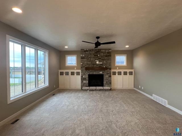 unfurnished living room with ceiling fan, a stone fireplace, a water view, and light carpet