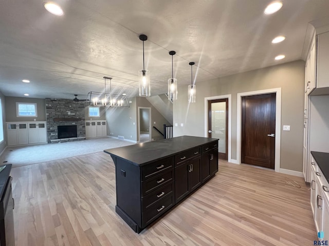 kitchen featuring a stone fireplace, white cabinetry, light hardwood / wood-style flooring, and decorative light fixtures