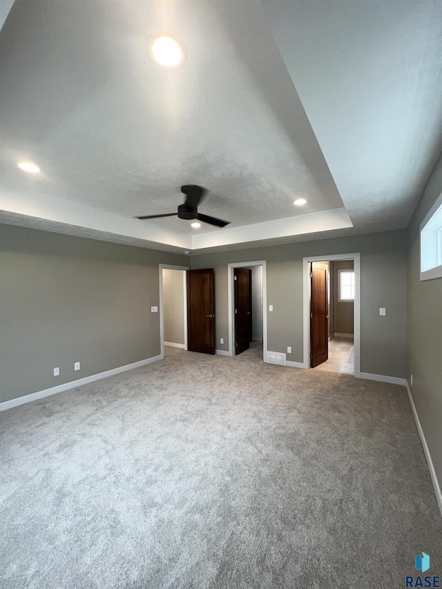 unfurnished bedroom featuring ceiling fan, light carpet, and a tray ceiling