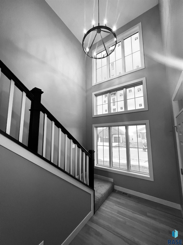 stairway with hardwood / wood-style flooring, plenty of natural light, a towering ceiling, and a chandelier