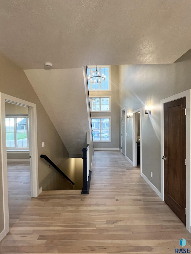 hallway featuring a textured ceiling, light hardwood / wood-style flooring, a chandelier, and vaulted ceiling