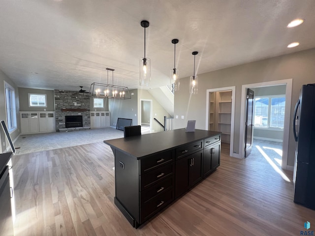 kitchen featuring light wood-type flooring, ceiling fan, pendant lighting, a stone fireplace, and fridge