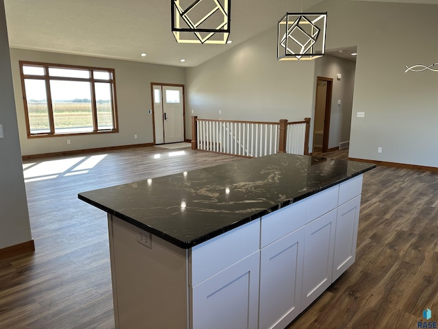 kitchen with dark hardwood / wood-style flooring, a kitchen island, pendant lighting, dark stone countertops, and white cabinetry