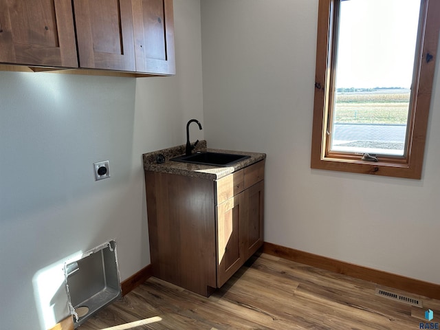 laundry room featuring hookup for an electric dryer, light hardwood / wood-style floors, cabinets, and sink