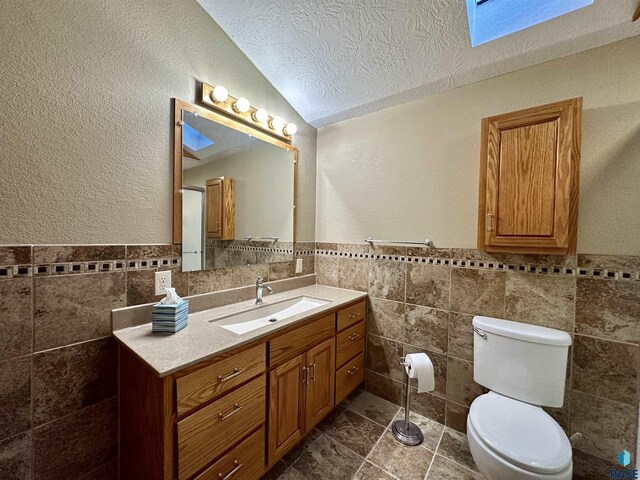 bathroom with toilet, lofted ceiling with skylight, vanity, a textured ceiling, and tile walls