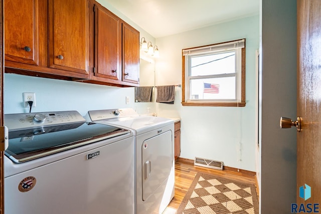 laundry room featuring washing machine and dryer, cabinets, and light wood-type flooring