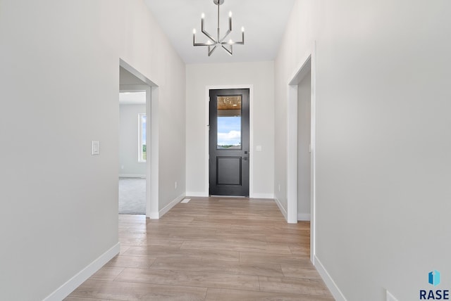 foyer entrance with a chandelier, light wood-style flooring, and baseboards