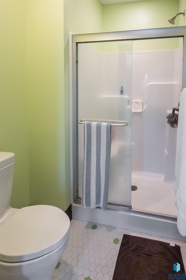 bathroom featuring tile patterned flooring, toilet, and a shower with shower door