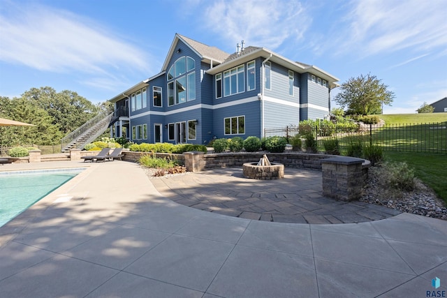 rear view of property featuring a fenced in pool, a patio, and an outdoor fire pit