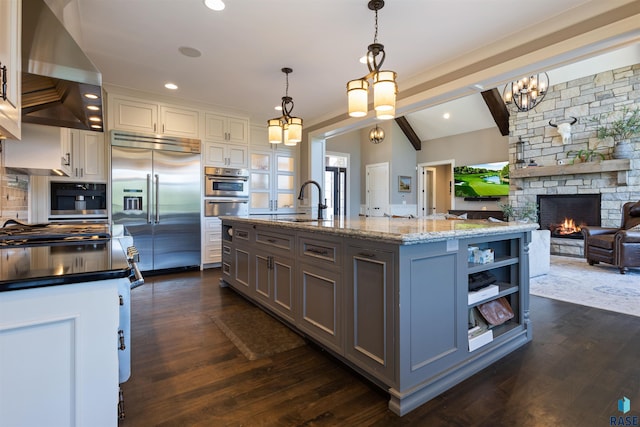 kitchen with hanging light fixtures, a stone fireplace, an island with sink, gray cabinets, and appliances with stainless steel finishes