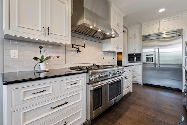 kitchen with tasteful backsplash, high end appliances, dark wood-type flooring, wall chimney range hood, and white cabinetry