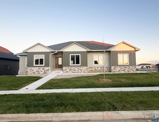 view of front of house featuring board and batten siding, stone siding, roof with shingles, and a front lawn