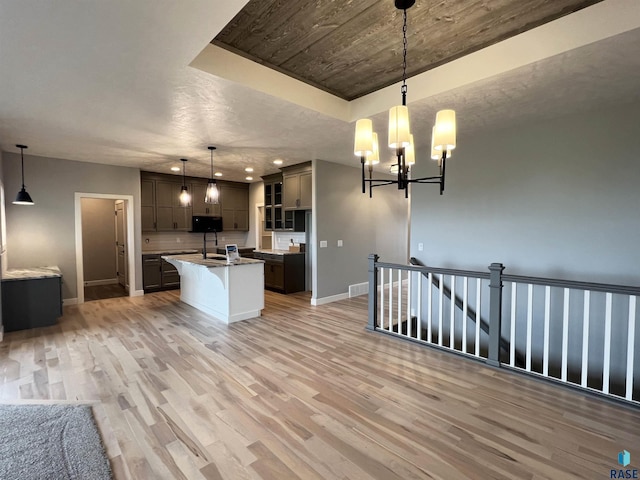 kitchen with hanging light fixtures, light hardwood / wood-style floors, and an island with sink