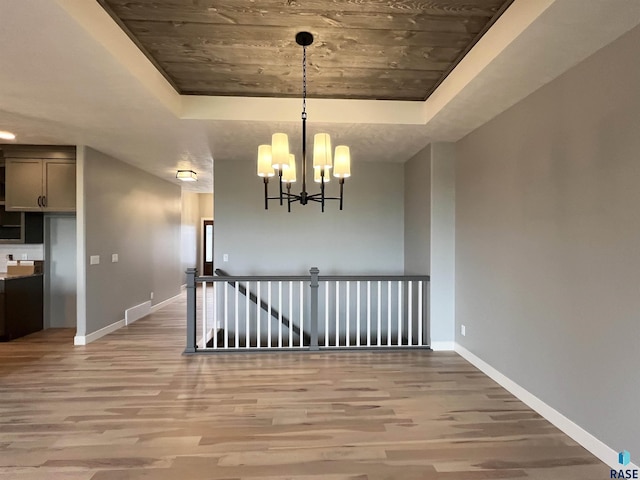 unfurnished dining area featuring a tray ceiling, hardwood / wood-style flooring, and a chandelier