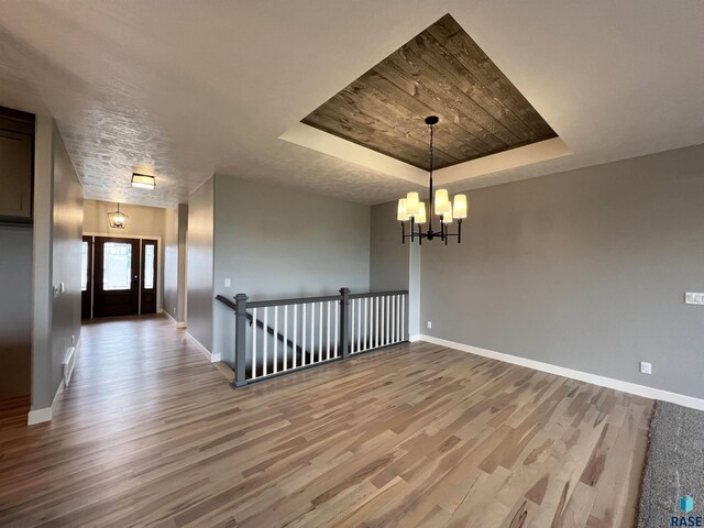 spare room with an inviting chandelier, a raised ceiling, and hardwood / wood-style flooring