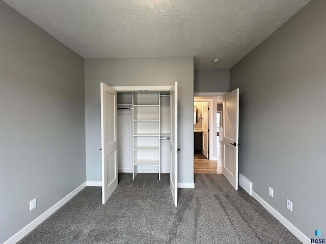 unfurnished bedroom featuring a textured ceiling, dark carpet, and a closet