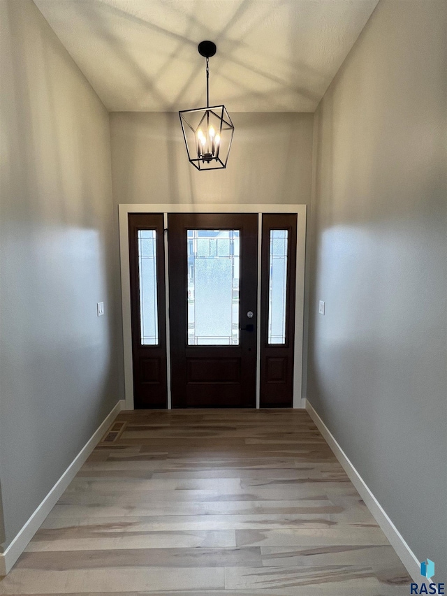 foyer featuring baseboards, light wood-style flooring, and a notable chandelier