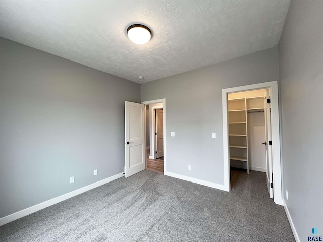 unfurnished bedroom with a closet, a spacious closet, dark carpet, and a textured ceiling