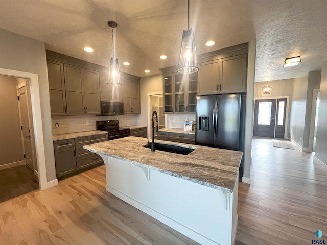 kitchen featuring sink, hanging light fixtures, light hardwood / wood-style flooring, appliances with stainless steel finishes, and light stone countertops