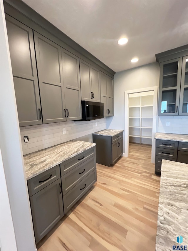 kitchen with tasteful backsplash, light stone counters, gray cabinets, and light wood-type flooring