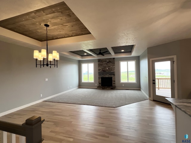 unfurnished living room featuring wood-type flooring, an inviting chandelier, a fireplace, and a tray ceiling