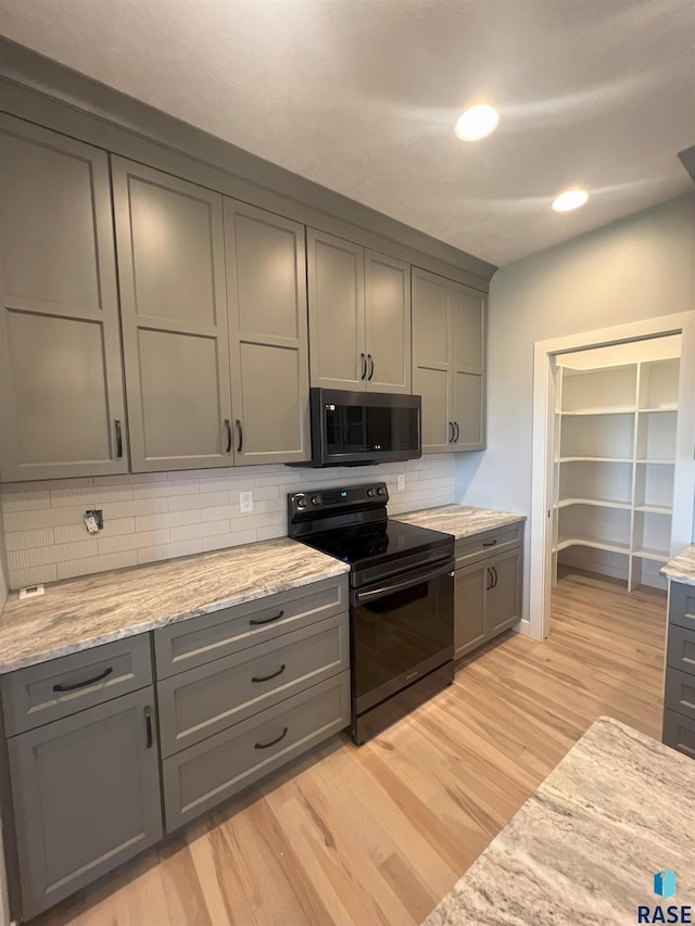 kitchen with gray cabinetry, light stone counters, black electric range, light hardwood / wood-style flooring, and backsplash