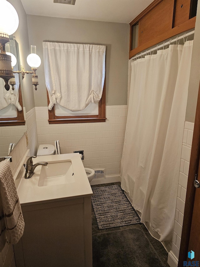 bathroom with walk in shower, vanity, toilet, and tile walls