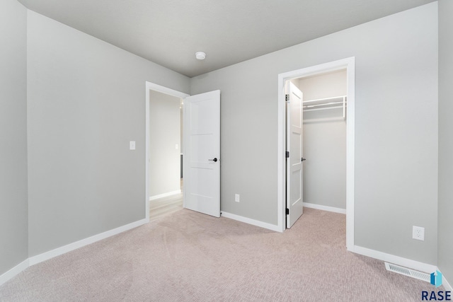 unfurnished bedroom featuring a spacious closet, light colored carpet, and a closet