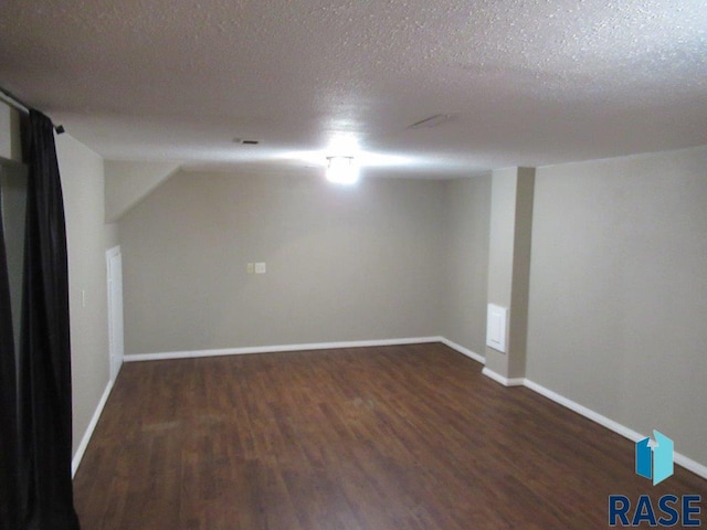 spare room with a textured ceiling, dark wood-style flooring, and baseboards