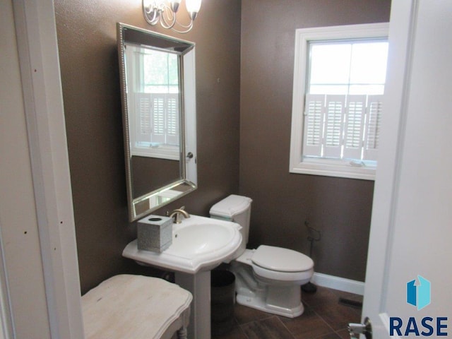 bathroom featuring a healthy amount of sunlight, baseboards, toilet, and a notable chandelier