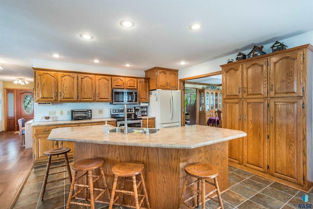 kitchen with stainless steel appliances, dark hardwood / wood-style flooring, an island with sink, a breakfast bar area, and a textured ceiling