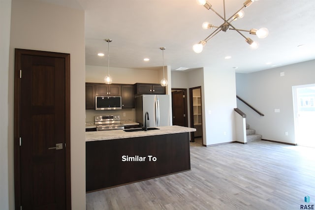 kitchen featuring appliances with stainless steel finishes, decorative light fixtures, sink, light stone countertops, and light hardwood / wood-style flooring