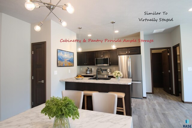 kitchen with appliances with stainless steel finishes, light hardwood / wood-style flooring, sink, pendant lighting, and light stone counters