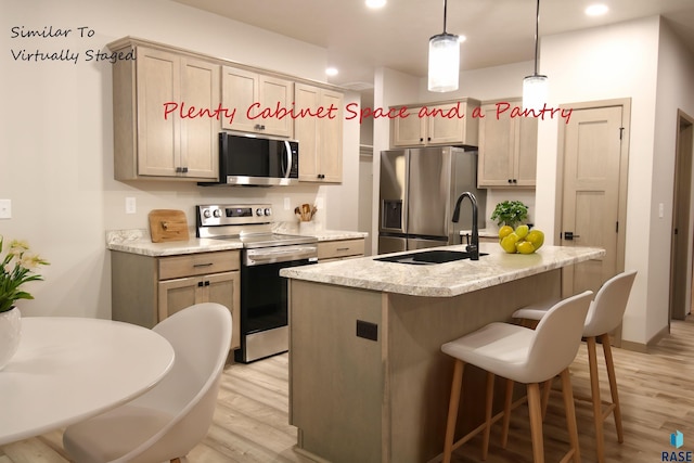 kitchen featuring appliances with stainless steel finishes, light wood-type flooring, a center island with sink, and a breakfast bar