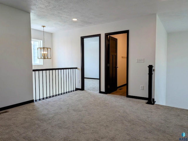 spare room with a chandelier, a textured ceiling, and carpet flooring