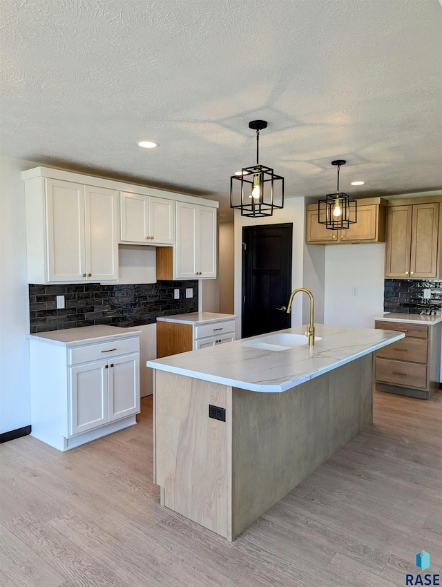 kitchen with light wood-type flooring, backsplash, pendant lighting, a kitchen island with sink, and sink