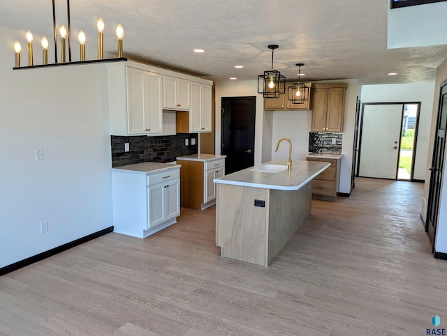 kitchen featuring light hardwood / wood-style floors, backsplash, sink, and an island with sink