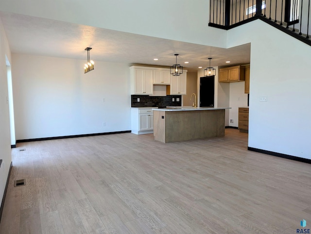 kitchen featuring sink, light wood-type flooring, white cabinetry, fridge, and a center island with sink