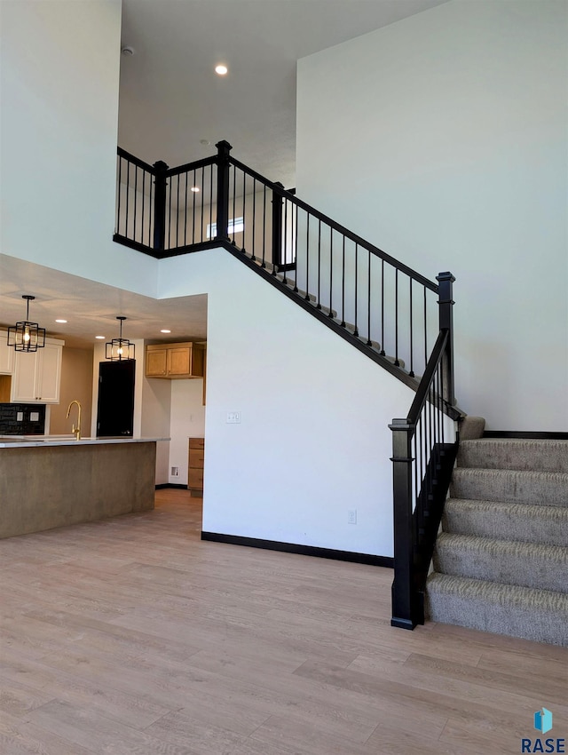 stairway with a towering ceiling, a notable chandelier, sink, and wood-type flooring