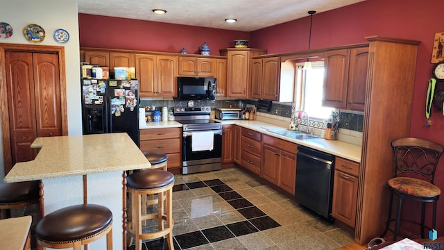 kitchen featuring sink, tasteful backsplash, a kitchen breakfast bar, pendant lighting, and black appliances