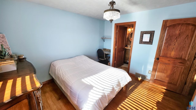 bedroom featuring dark hardwood / wood-style floors, connected bathroom, and a chandelier