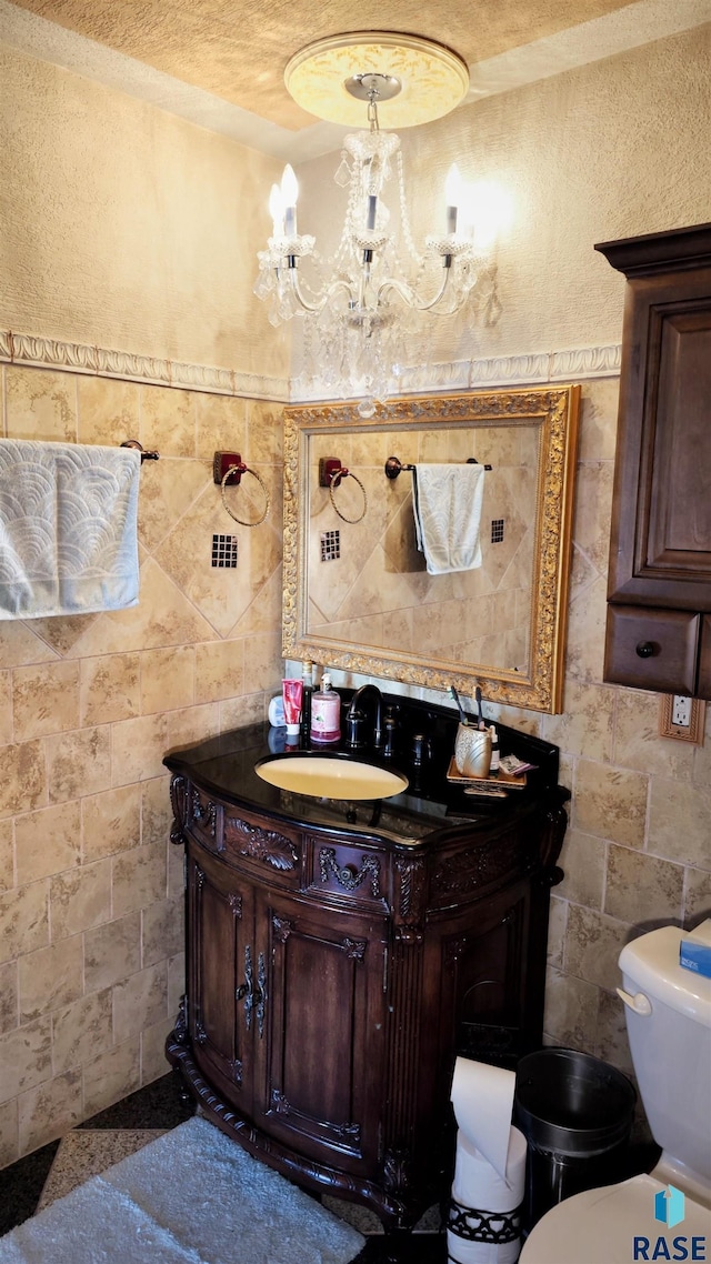 bathroom featuring vanity, toilet, a chandelier, and tile walls