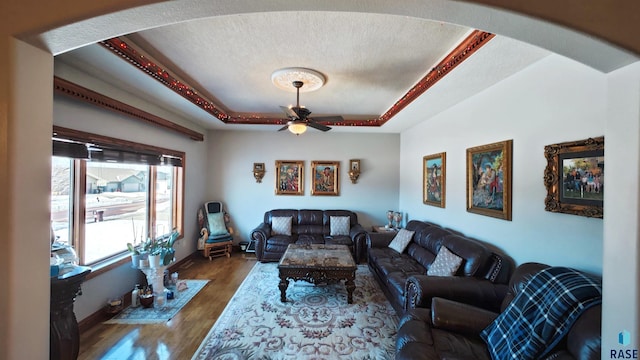 living room featuring dark wood-type flooring, ceiling fan, a raised ceiling, and a textured ceiling