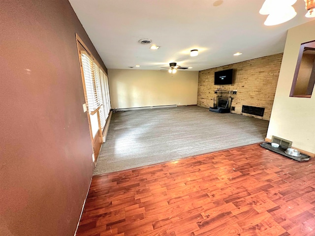 unfurnished living room with a large fireplace, a baseboard radiator, ceiling fan, and hardwood / wood-style floors