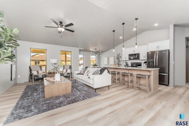 living room featuring ceiling fan with notable chandelier, sink, vaulted ceiling, and light wood-type flooring