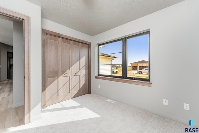 unfurnished bedroom with light carpet, a textured ceiling, and a closet