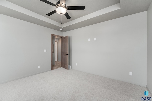 empty room with a raised ceiling, ceiling fan, and light colored carpet