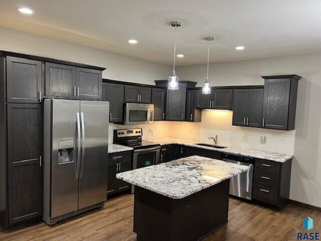 kitchen with appliances with stainless steel finishes, a center island, hanging light fixtures, and hardwood / wood-style floors