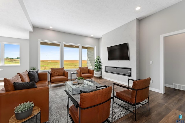 living room with recessed lighting, visible vents, dark wood-type flooring, a glass covered fireplace, and baseboards